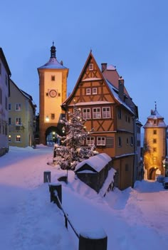 a small christmas tree in the middle of a snow covered street with two tall buildings