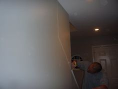 a man is painting the wall in his house with white paint and an electric brush