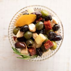 a glass bowl filled with olives, orange slices and other food items on top of a wooden table