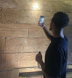 a man holding up a smart phone in front of a stone wall