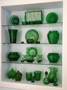 green glass vases and dishes are on display in a white cabinet with glass shelves