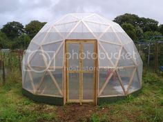 a small greenhouse in the middle of a field with lots of plants and trees around it