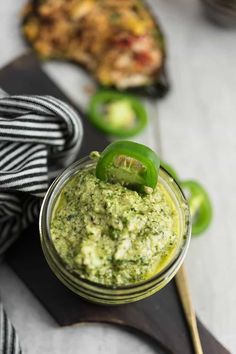 a small jar filled with green sauce on top of a cutting board next to other food items