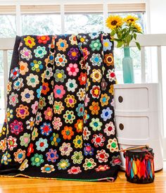 a black blanket with multicolored flowers on it next to a vase and flower pot