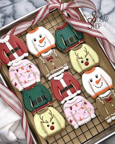 decorated cookies in the shape of sweaters and snowmen on a cookie sheet with ribbon