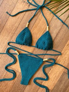 two pieces of crocheted bikinisuit on wooden floor next to palm tree branch