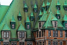 an old brick building with green roof and steeples on it's sides in the rain