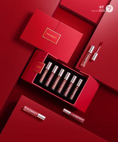 an open box with four lipsticks in it on a red surface next to other items