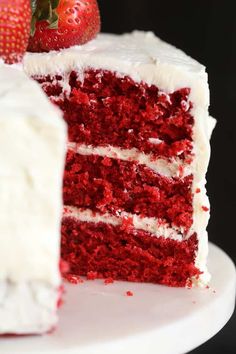 a slice of red velvet cake with white frosting and strawberries on the side