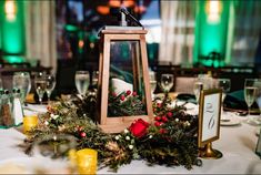 a small lantern on top of a table with greenery and candles in front of it