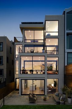 an exterior view of a modern house at night with lights on the windows and furniture in the yard