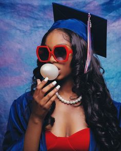 a woman wearing red glasses and a graduation cap is holding an egg in front of her face