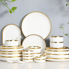 white and gold dinnerware set on table with green plant in the corner behind it