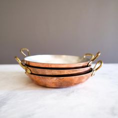 three metal bowls sitting on top of a white countertop next to each other with gold handles