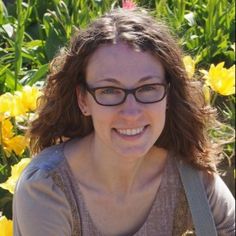 a woman with glasses is smiling in front of some yellow tulips and pink flowers