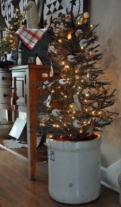 a small christmas tree in a white pot on the floor next to a dresser and mirror