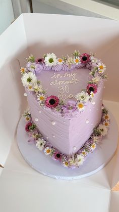 a heart shaped cake sitting on top of a white box with flowers around the edges