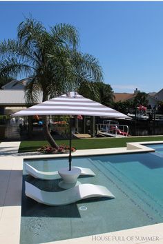 an umbrella sitting on the side of a swimming pool next to a palm tree and house