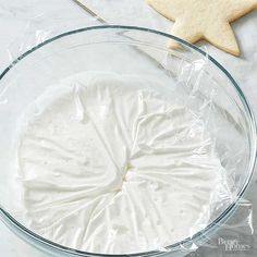 a glass bowl filled with white icing next to a star shaped cookie