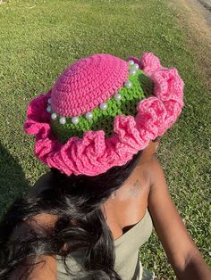 a woman sitting in the grass wearing a pink hat with green and white flowers on it