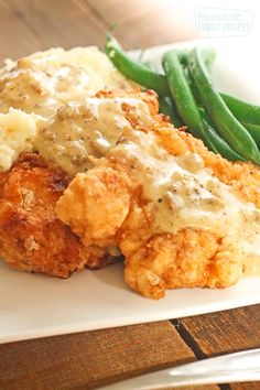 chicken with gravy and green beans on a white plate next to a fork