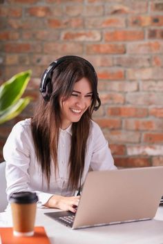 a woman sitting at a table with a laptop and headphones in her ears smiling