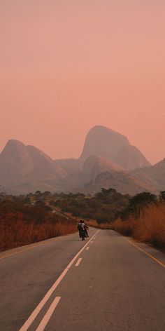 a motorcycle parked on the side of a road in front of some mountains at dusk