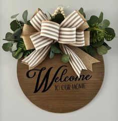 a welcome sign hanging on the side of a wall with greenery and bow around it