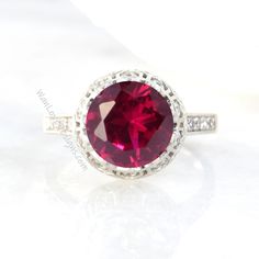 a ring with a large red stone surrounded by white diamonds on a plain surface,