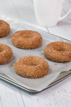 six donuts on a baking tray next to a cup of coffee