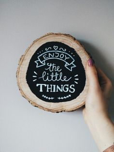 a hand holding a piece of wood that says enjoy the little things