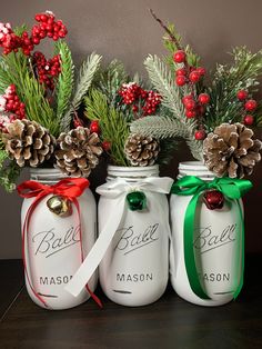 three mason jars decorated with pine cones and holly