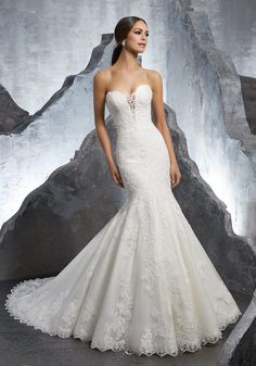 a woman in a white wedding dress standing next to some large rock formations and posing for the camera