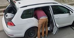 two people standing in the back of a white car with their hands on the open hatchback door