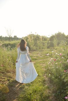 a woman in a white dress walking through a field