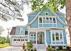 a blue house with white trim on the front and side of it, surrounded by trees