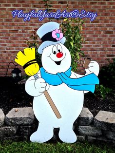 a snowman holding a broom standing in front of a brick wall