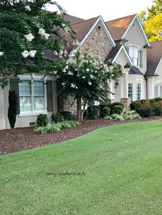 a house that is in the grass near some bushes and trees with white flowers on them