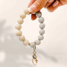 a person holding onto a beaded bracelet with white beads and gold accents on it