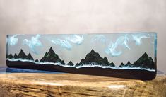 a wooden table topped with a glass vase filled with water and mountains covered in clouds