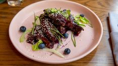 a white plate topped with meat covered in sauce and blueberries next to a glass of water