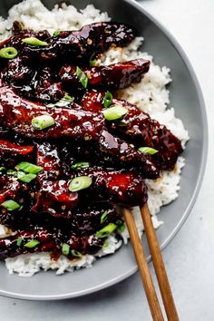 a plate with rice, meat and sauce on it that has chopsticks in it