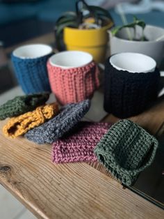 several knitted cups are sitting on a table next to two mugs and a plant