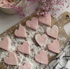 heart shaped cookies on a cutting board with powdered sugar and flowers in the background