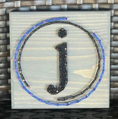 a wooden sign with the letter j on it and some beads hanging from it's sides