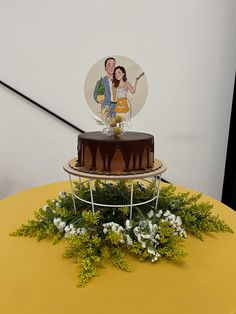 a cake on a yellow table with white flowers and greenery