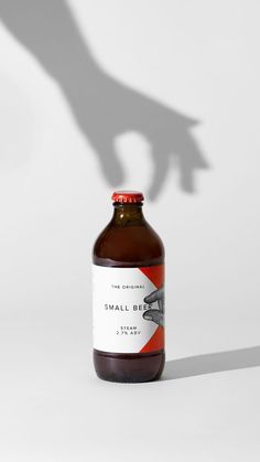 a bottle of small brown liquid sitting on top of a white table next to a person's shadow