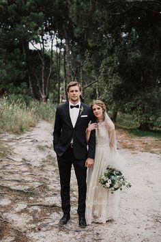 a bride and groom standing on a path in the woods