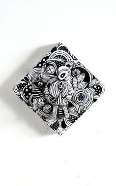 a black and white square object on a white surface with an intricate design in the center