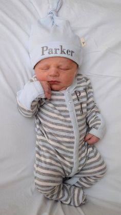 a baby laying on top of a white bed wearing a striped outfit and a hat